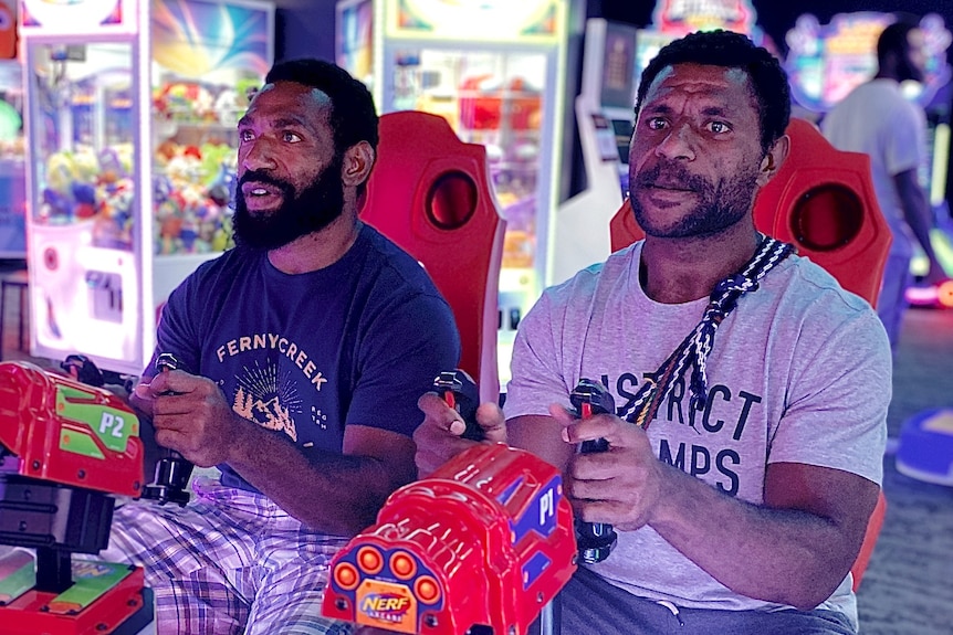Two men play video games in an arcade.