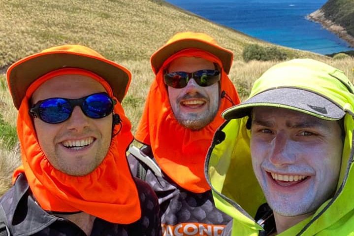 Three men smile at the camera while wearing sun huts, sunglasses and zinc sunscreen