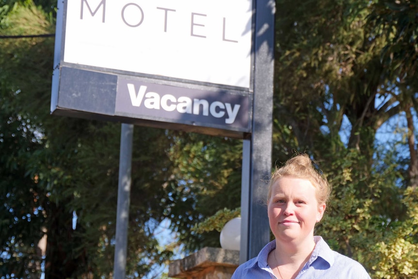 A woman stands in front of a motel sign that says 'vacancy'.
