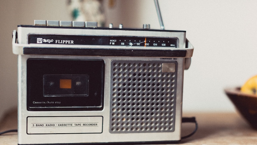 A silver radio and tape player and antenna sits on a bench next to a bowl of fruit