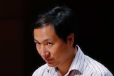 Disgraced Chinese scientist He Jiankui pictured onstage against black backdrop