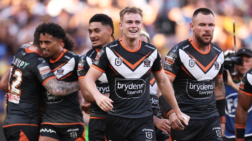 Lachlan Galvin leads a group of smiling Wests Tigers players.