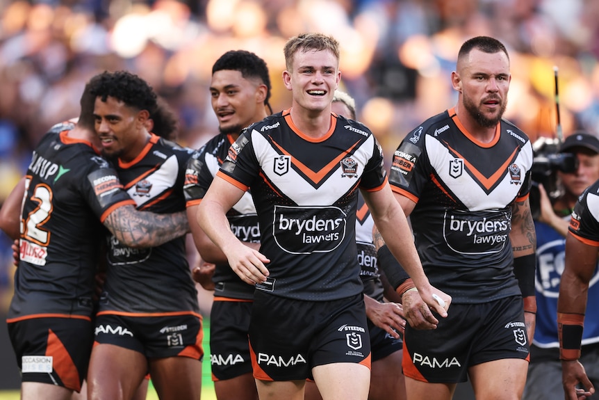 Lachlan Galvin leads a group of smiling Wests Tigers players.