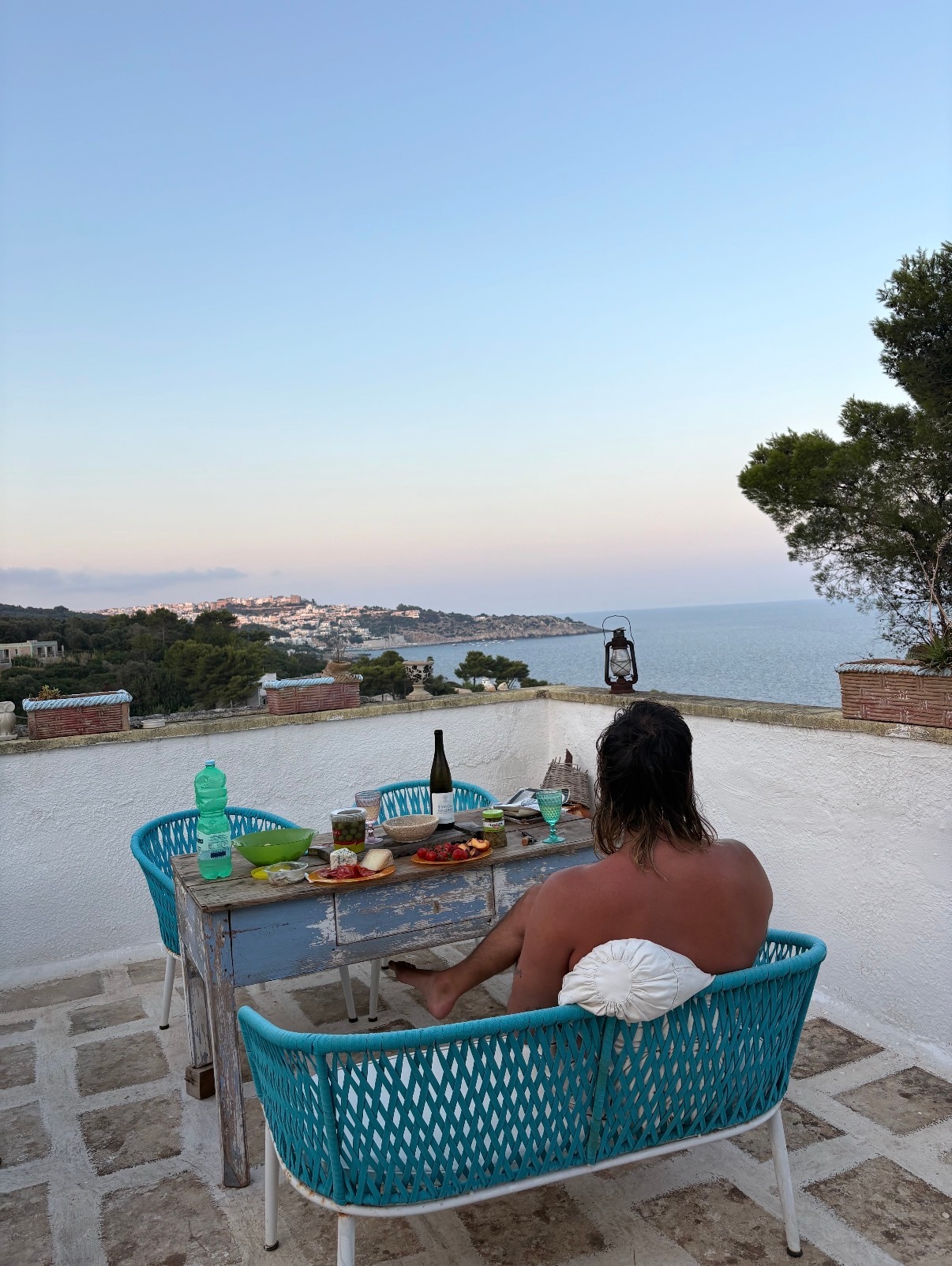 Mitch Brown está sentado de costas para uma varanda pitoresca, olhando para um pôr do sol rosa sobre o oceano
