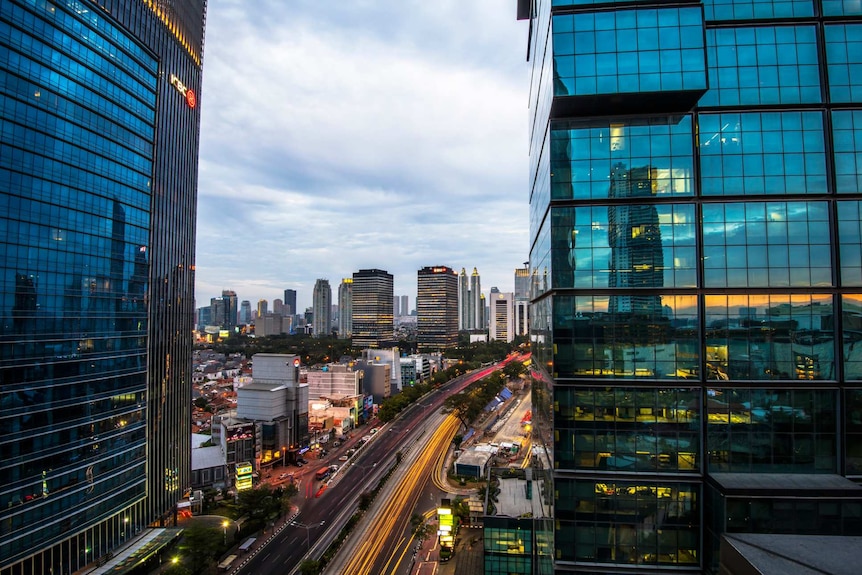 From a high vantage point, you look down on a freeway running through blue-tinted high-rises in Jakarta.