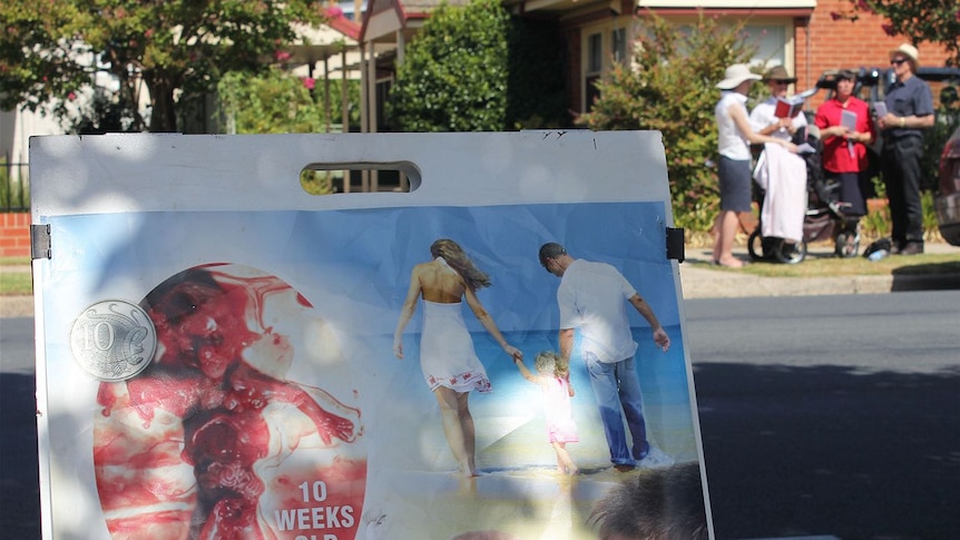 A group of anti-abortion protesters with a graphic poster showing a 10 week old fetus outside a clinic.