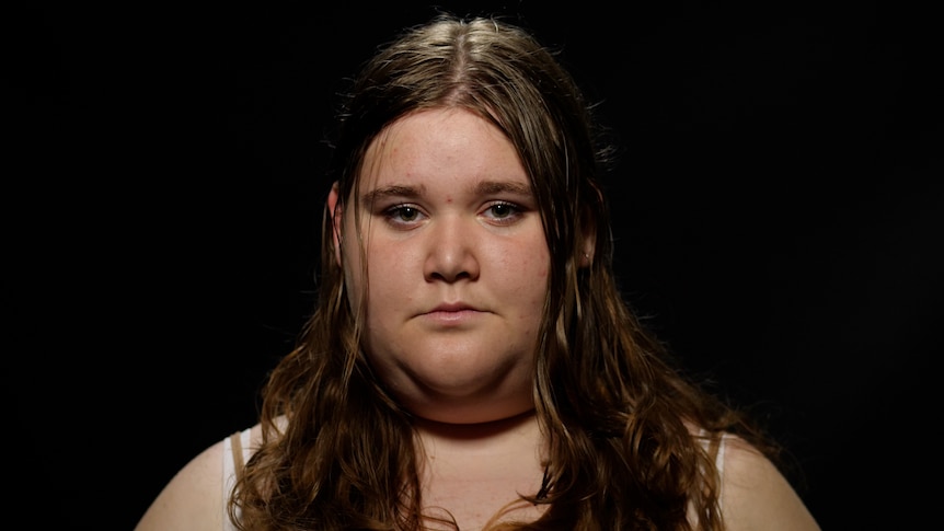 A young woman with light brown hair looking at camera. Black background.