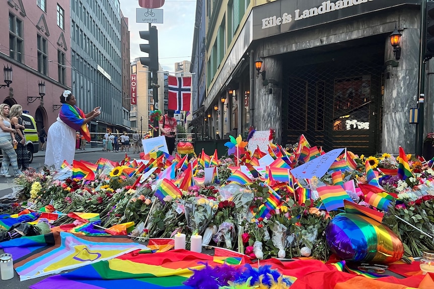 A woman takes a photo of flowers and rainbow flags left as tributes to victims