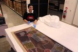 Berndt Museum curatorial assistant Sarah Ridhuan inspects a large Aboriginal dot painting  on a table.