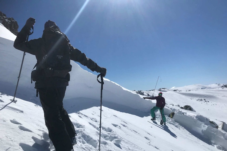 Two people look at a sharp ice wall that is the crown of an avalanche.