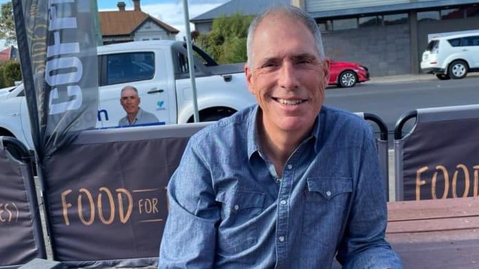 A balding man smiles as he sits at a cafe