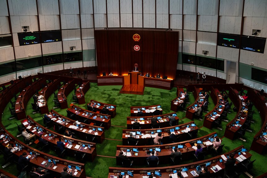 Politicians sit behind desks in a round room with green carpet