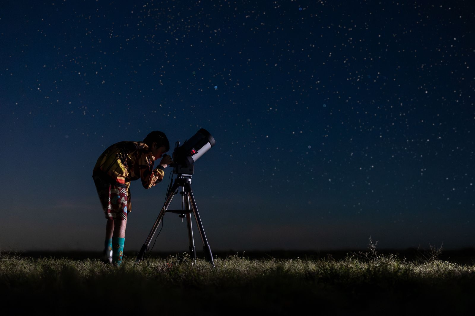 A silhouetted person looks into a telescope on a dark night.