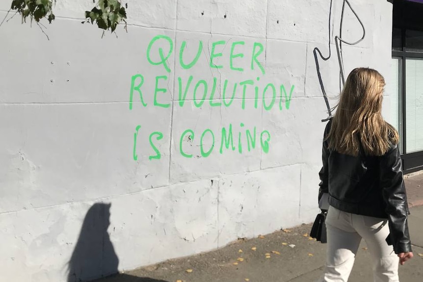 A woman walks past a wall in Kyiv with graffiti saying "Queer revolution is coming". 