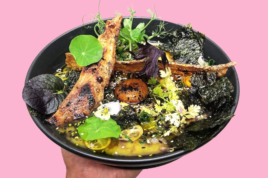 Person's hand holding a large bowl of salmon with cured yolk and seaweed toppings