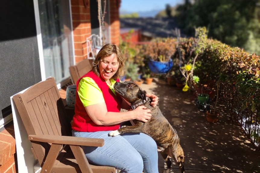 Mel laughs as a dog puts its nose towards her. They're outside in the sunshine.