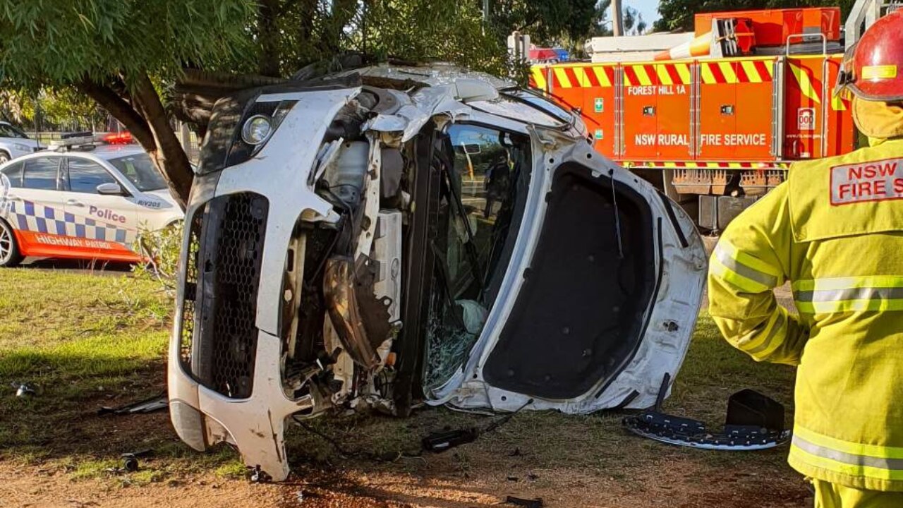 Image of white car on its side seriously damaged with emergency services in rear.
