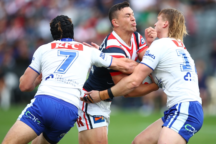 A Sydney Roosters NRL player is tackled by two Canterbury opponents.