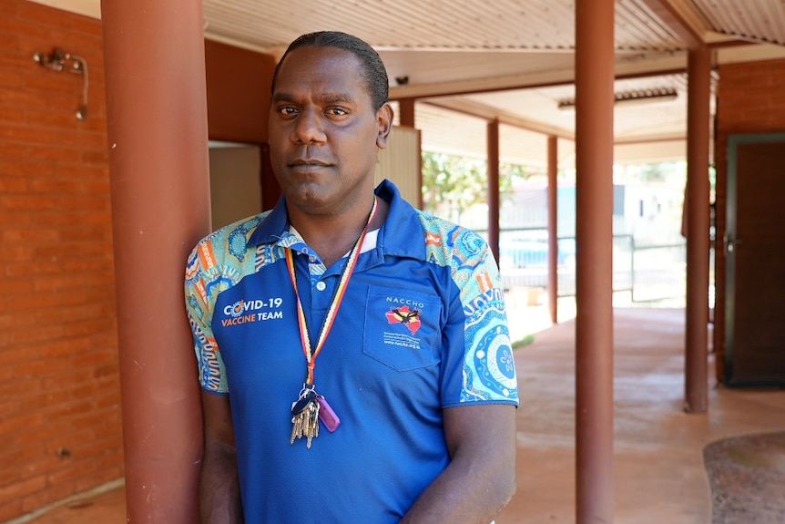 An Aboriginal man in a colourful shirt stands next to a pole