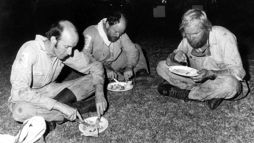 Firefighters sit on a lawn eating dinner