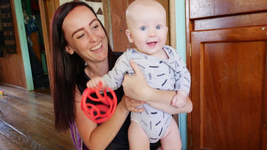 A mother and her baby standing on her lap bight eyed and smiling.