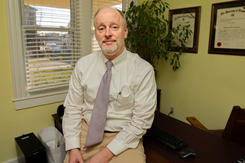 A man in a tie leaning against a desk