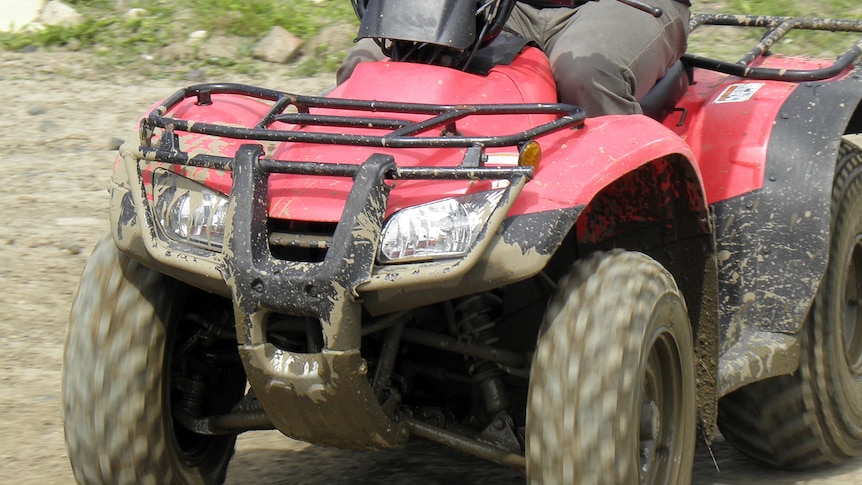 A close up of a person riding a red quad bike covered in mud.