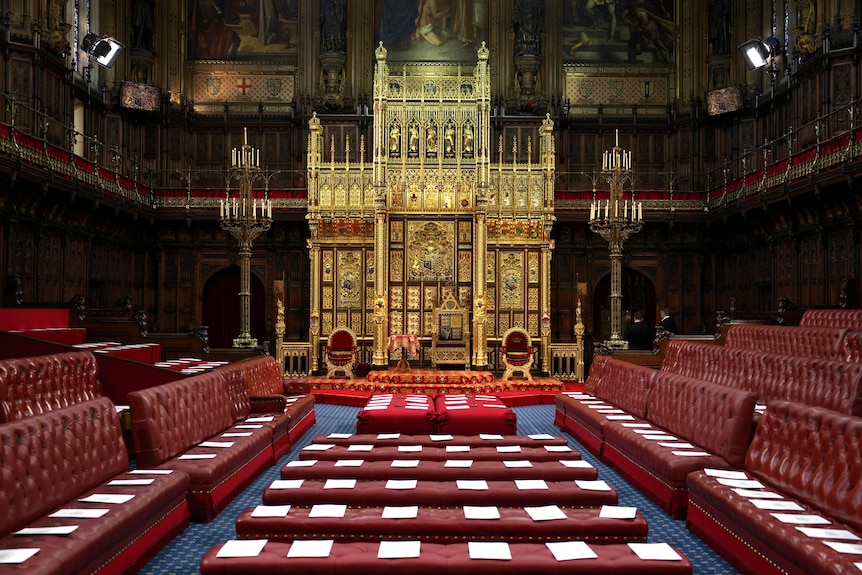An ornate gold throne at the end of a large hall filled with ornate red leather seating