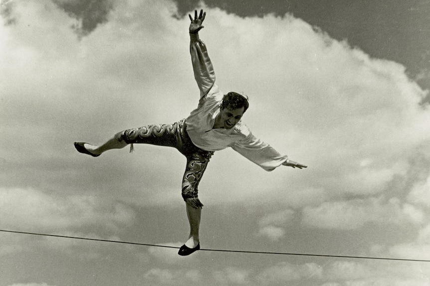 A black and white photo of a man on a wire and clowns underneath