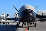 Ground crew rush to a space craft similar to a space shuttle parked on a runway after landing.