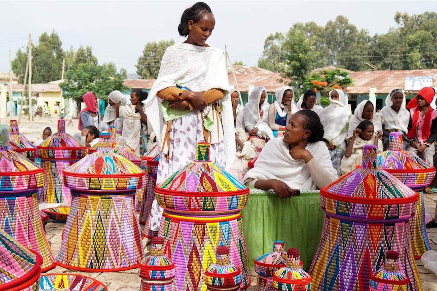 Two women standing among brightly-coloured weaved baskets.