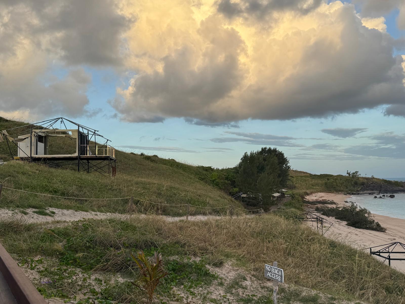 Foto del paisaje de una playa, la costa a la derecha de la imagen, de un bungalow en la colina sólo quedan los marcos de los andamios.
