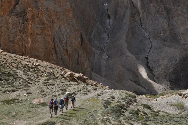 With huge mountains ahead of them, a small group of people is just visible in the middle of arid land.