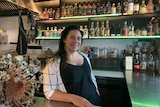 A woman stands in front of shelves of bottles in a bar.
