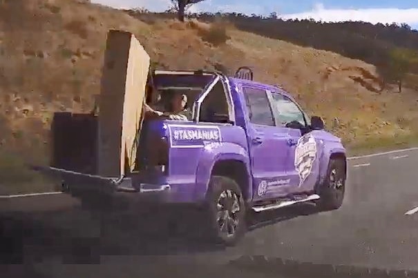 Dash cam still showing person holding item in tray of ute on highway.