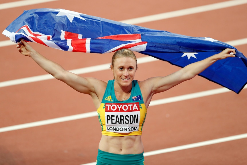 Sally Pearson on an athletics track holding the Australian flag above her head.