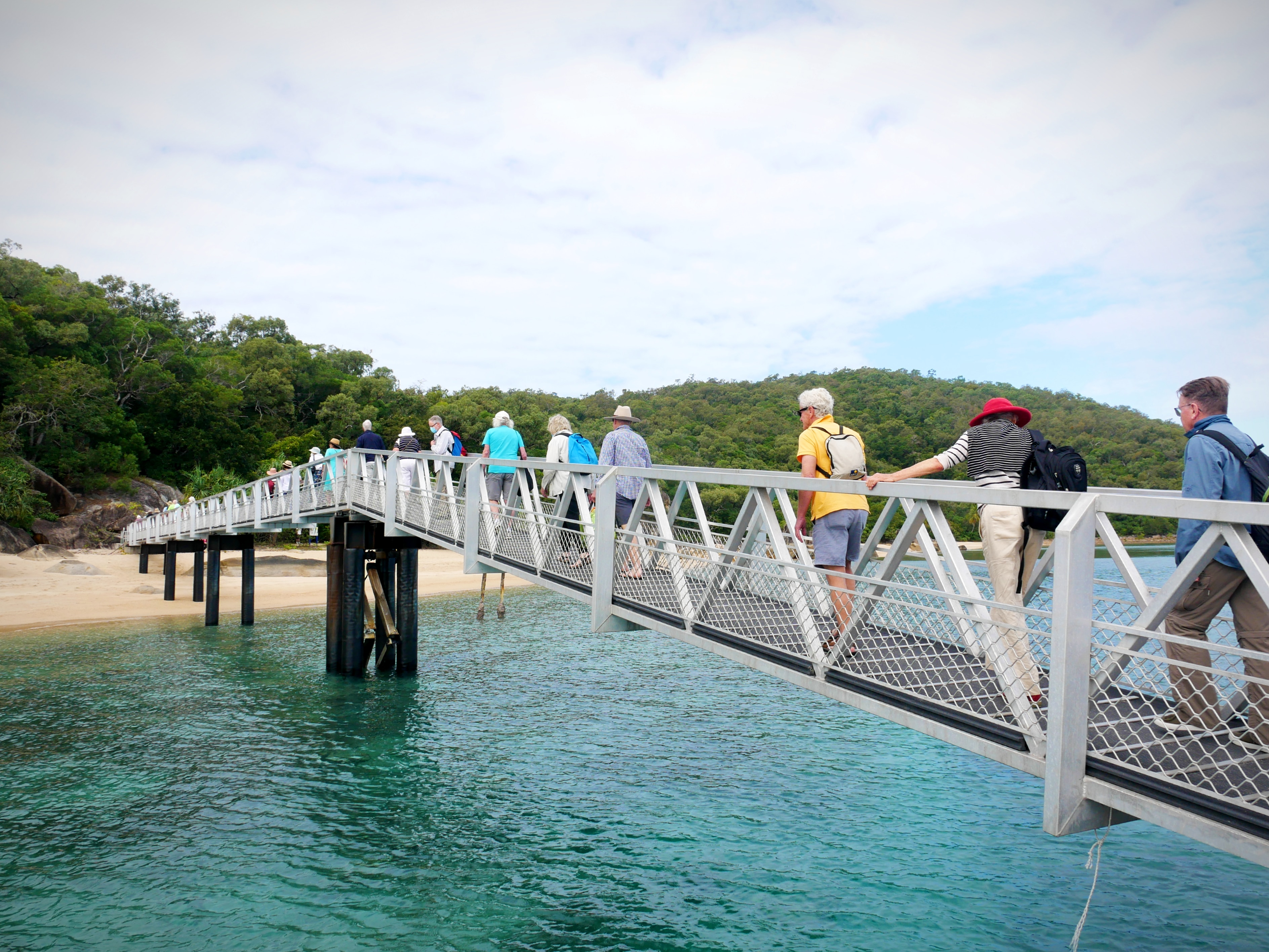 People walk across a long bridge to arrive on a sandy island beach