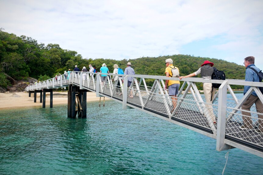 People walk across a long bridge to arrive on a sandy island beach