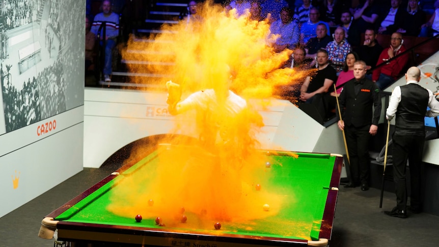 Orange powder explodes as a protester throws it while kneeling on a snooker table.
