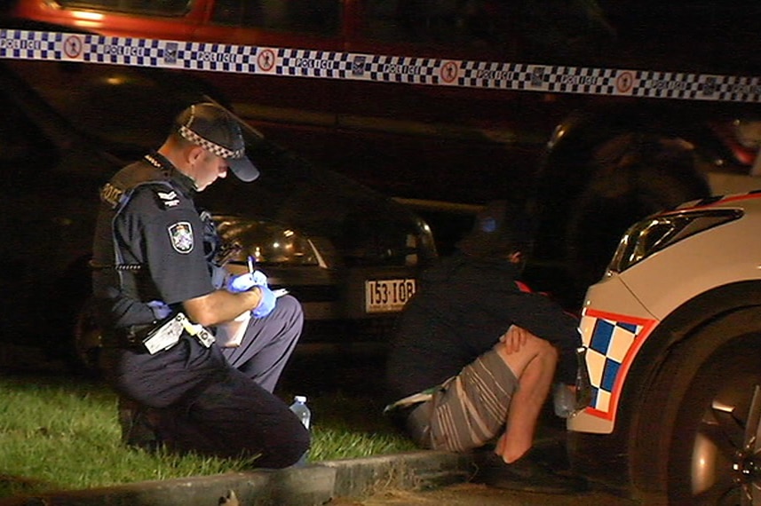 A police officer writes in his notebook while a witness sits in the gutter of a Petrie street where a man was shot in the chest.