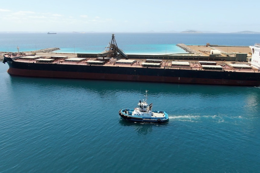 A blue tug boat driving past a large black ship