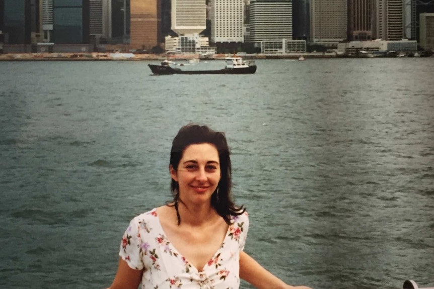 Mid twenty-something year old sue lannin wears a pink floral dress as she stands near the bay overlooking the hong kong city