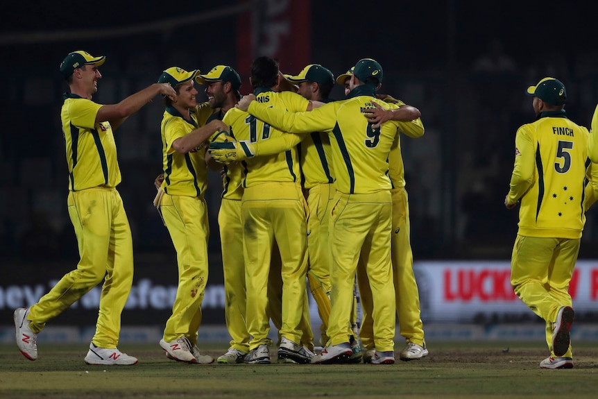 Australia's players celebrate beating India by gathering in a huddle.