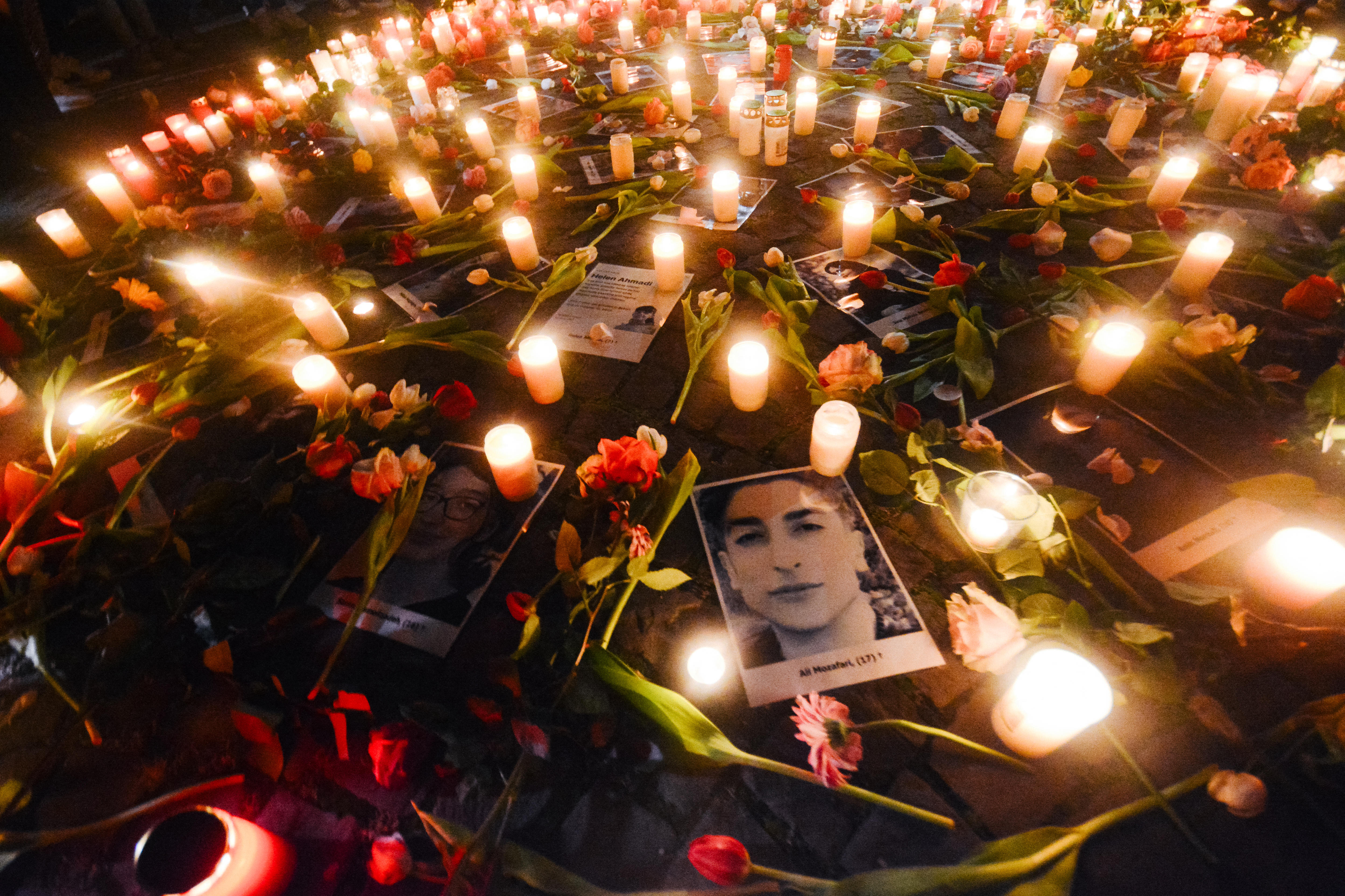 Candles, flowers and photos lay on the ground in a circle  at a candlelight vigil.