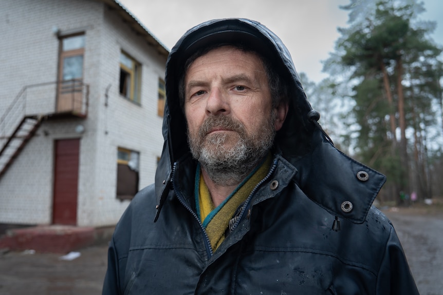 A man in a hooded parka standing outside a building, looking haunted 