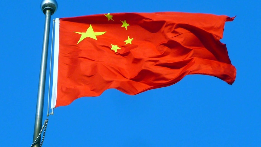 The Chinese flag flies in front of a blue sky.