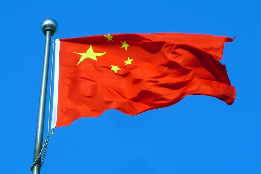 The Chinese flag flies in front of a blue sky.