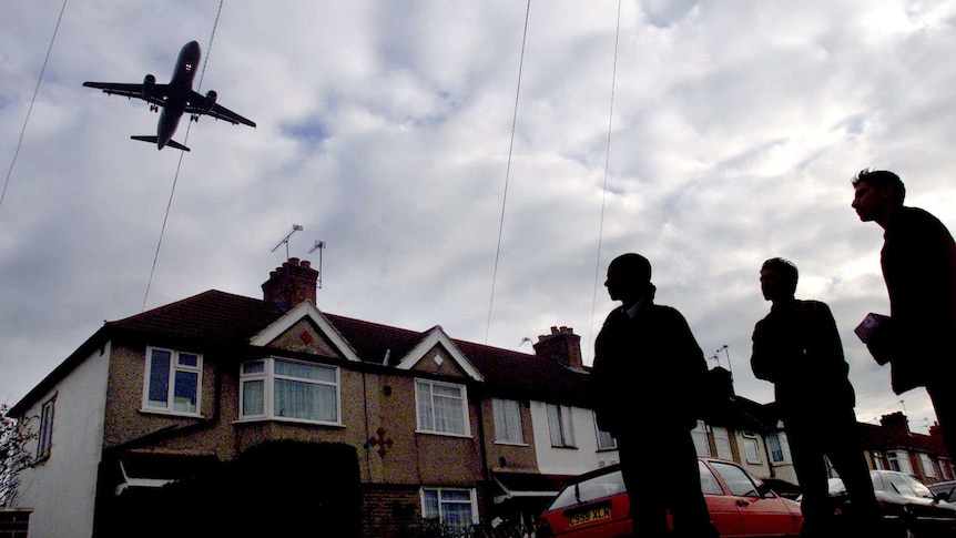 Young Hounslow residents on their way to school watch as a plane bound for London's Heathrow airport flies low over houses.