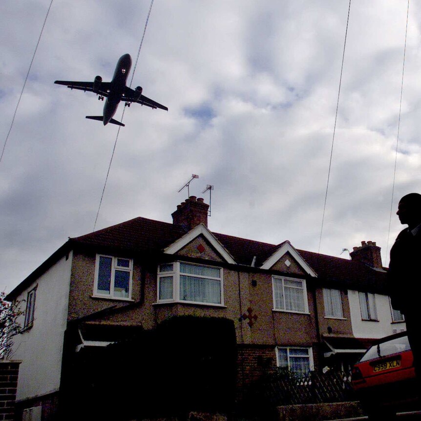 Young Hounslow residents on their way to school watch as a plane bound for London's Heathrow airport flies low over houses.
