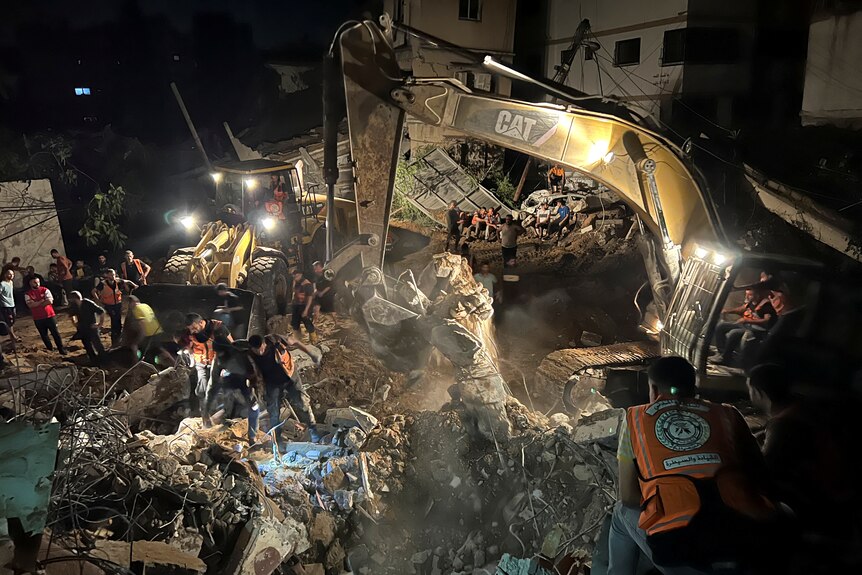 Palestinian rescuers, including a excavator,  working at night to search for casualties under a rubble